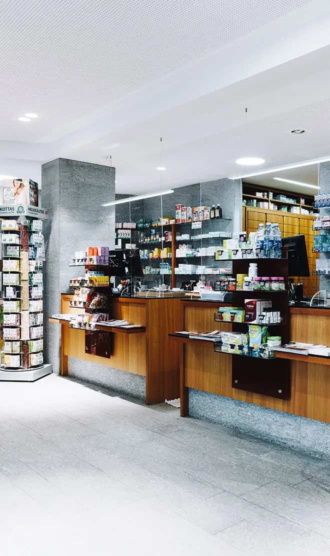Eine moderne Apotheke mit Regalen mit verschiedenen Produkten, einem Holztresen und heller Beleuchtung. Der Boden ist hell, und die Atmosphäre wirkt sauber und organisiert.