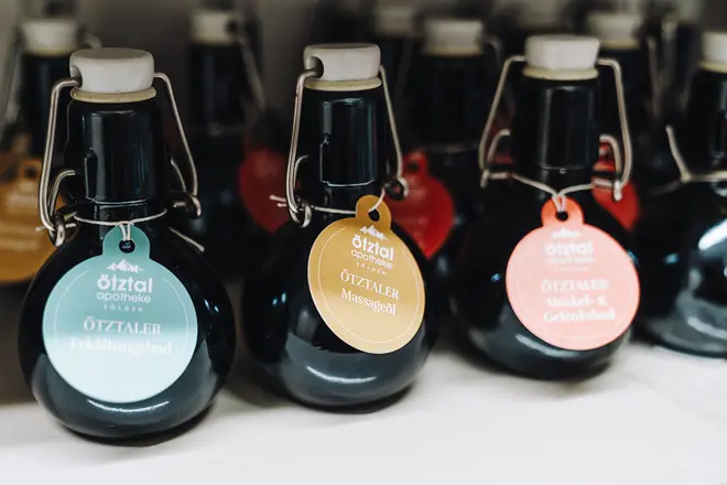 Mehrere dunkle Glasflaschen mit Bügeldeckeln sind in einer Reihe angeordnet. An jeder Flasche hängt ein buntes, rundes Etikett, das auf die verschiedenen Arten von Inhalt hinweist. Die Etiketten sind blau, gelb und rot.