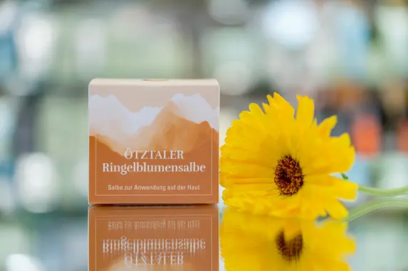 Eine bunte Verpackung steht neben einer leuchtend gelben Blume vor einem verschwommenen Hintergrund.