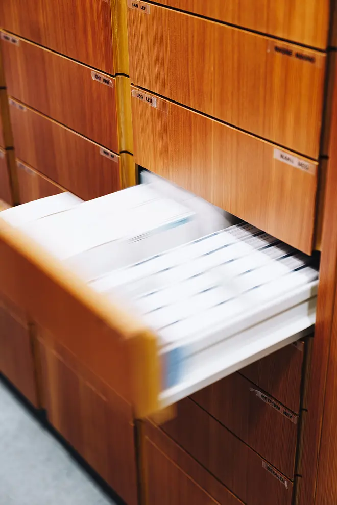 Eine Schublade eines hölzernen Medikamentenschranks ist teilweise geöffnet und gibt den Blick auf ordentlich geordnete Verpackungen frei. Die umliegenden Schubladen bleiben geschlossen.
