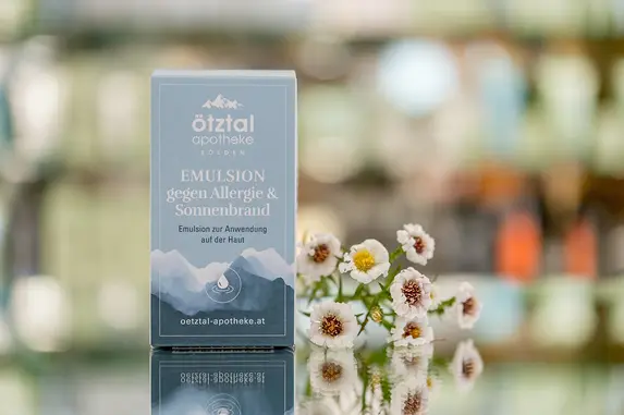 Eine hellblaue Verpackung steht neben einem kleinen Strauß weißer Gänseblümchen vor einem sanft verschwommenen Hintergrund. Gezeigt wird ein Produkt der Eigenherstellung.